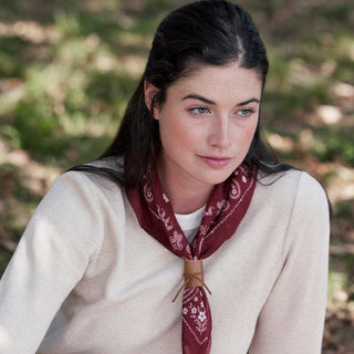 A woman outdoors wearing a cream knit sweater and a dark red paisley neck scarf tied at the collar.