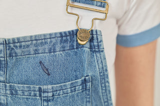 Brass-colored button and buckle on denim overall bib
