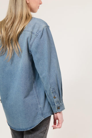 Person wearing a light blue denim shirt on a plain background