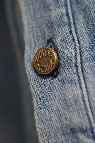 Close-up of a denim jacket with a gold button labeled 'Annie Ozark'.