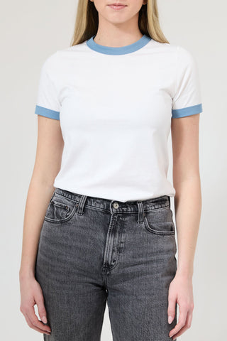 Person wearing a white t-shirt with blue trim and gray jeans on a plain background