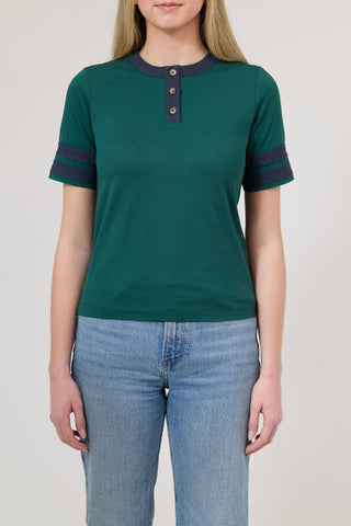 Person wearing a green short-sleeve shirt with navy accents and blue jeans on a plain background
