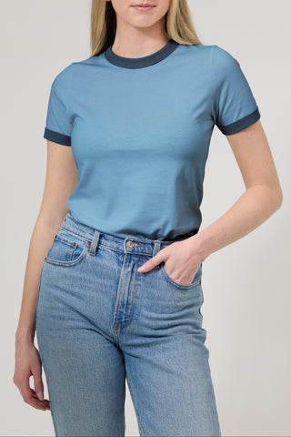 Person wearing a blue t-shirt with dark trim and high-waisted jeans on a plain background