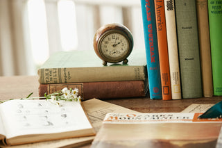 Stack of books with an alarm clock on top, placed on a wooden surface.