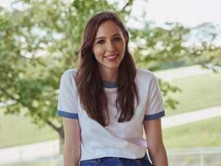 Woman wearing a white and blue shirt with a blurred green outdoor background