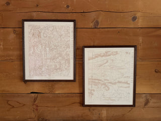 Two framed vintage maps with dark brown frames hanging on a rustic wooden wall.