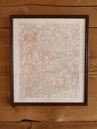A framed vintage topographical map of 'Mackay Plateau' with fine black and red line details on an off-white background, enclosed in a dark brown wooden frame and mounted on a rustic wooden plank wall.
