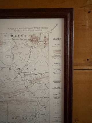 A framed vintage-style topographic map of the Arkansas Indian Territory, shown hanging on a wooden wall. The map includes contour lines, labeled regions, and a legend panel, enclosed in a dark wood frame.