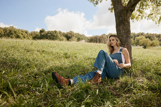 Woman sitting under a tree in a grassy field on a sunny day