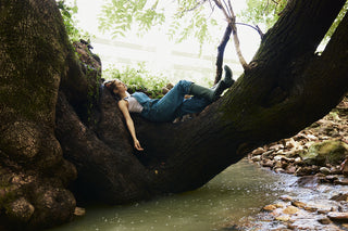 Person lying on a large tree root over a stream in a forest