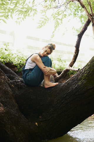 Person sitting on a large tree trunk by a body of water with greenery in the background