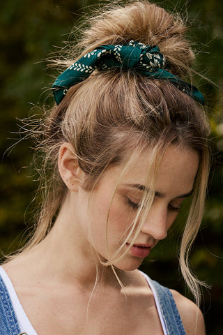 Woman with a bun and green headband against a blurred natural background