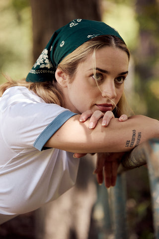 Woman with a green bandana and leaning against a tree