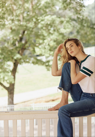 Woman sitting on a railing outdoors with trees in the background